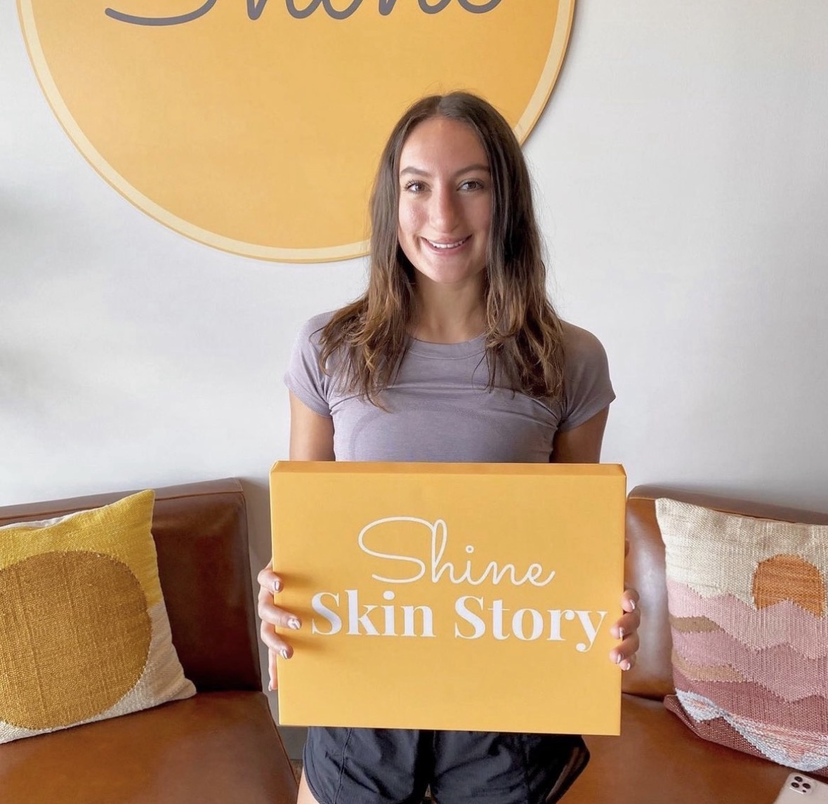 A smiling Shine member holding a yellow Shine Skin Story box