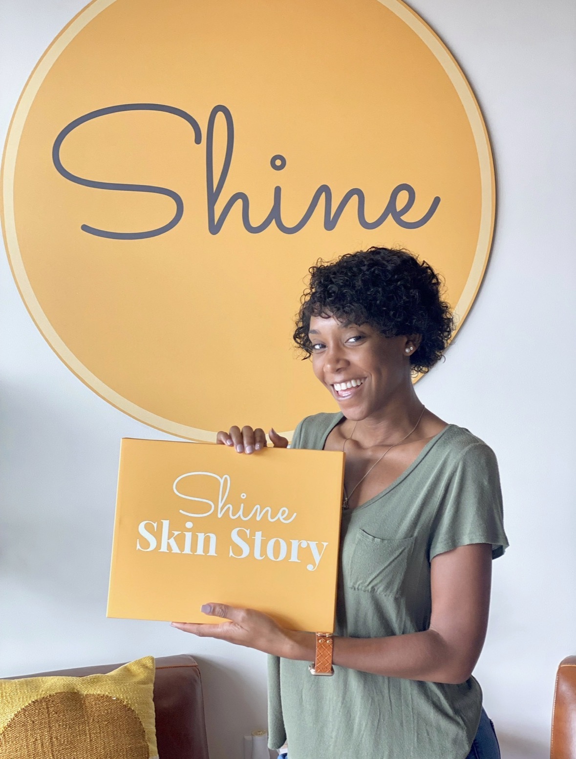 A happy Shine member holding a Shine Skin Story box in front of the Shine logo wall